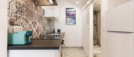 A narrow kitchen with patterned tiles, a coffee machine, and a refrigerator.