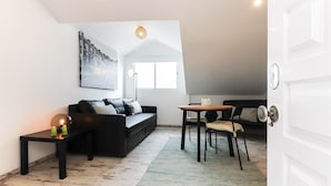A modern living room with a black sofa, a small table, and a chair. There is a painting on the wall, a window, and a door. - Bairro Alto Views by Homing (Lisbon)