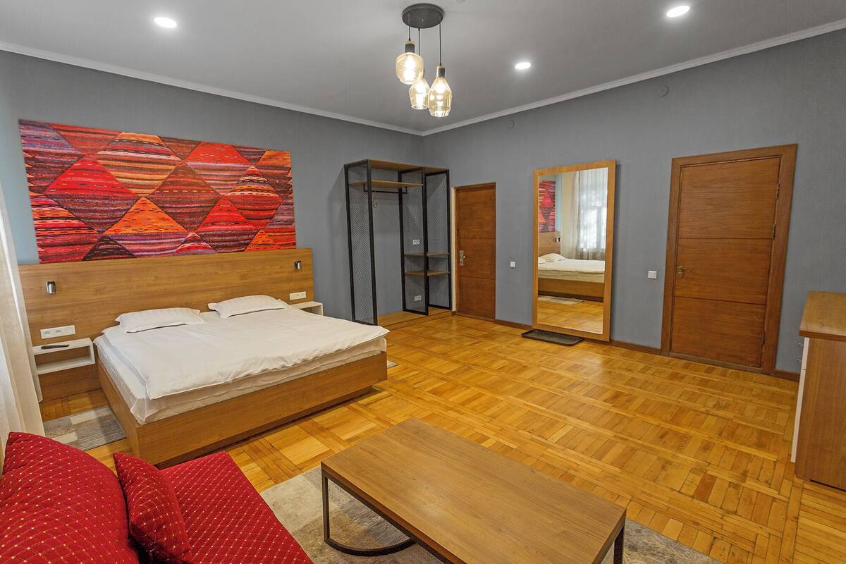 A bedroom with a wooden bed, a red sofa, a wooden table, and a large mirror.