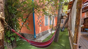 A hammock in a courtyard with a stone wall, a wooden deck, and a building with decorative plates. - Koisha Hostel (Bishkek)