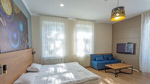 A modern bedroom with a large bed, a sofa, a coffee table, and a TV. - Koisha Hostel (Bishkek)