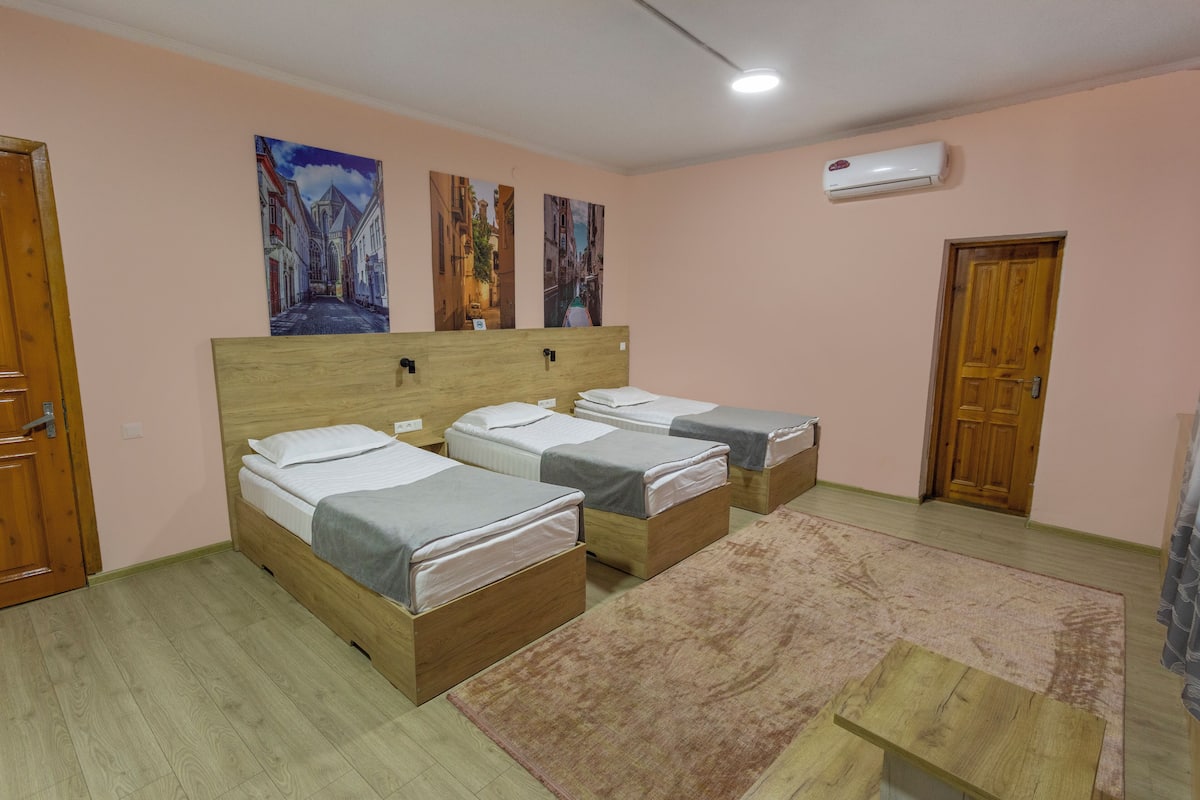 A room with three wooden beds, a wooden bench, a pink wall, and a door.