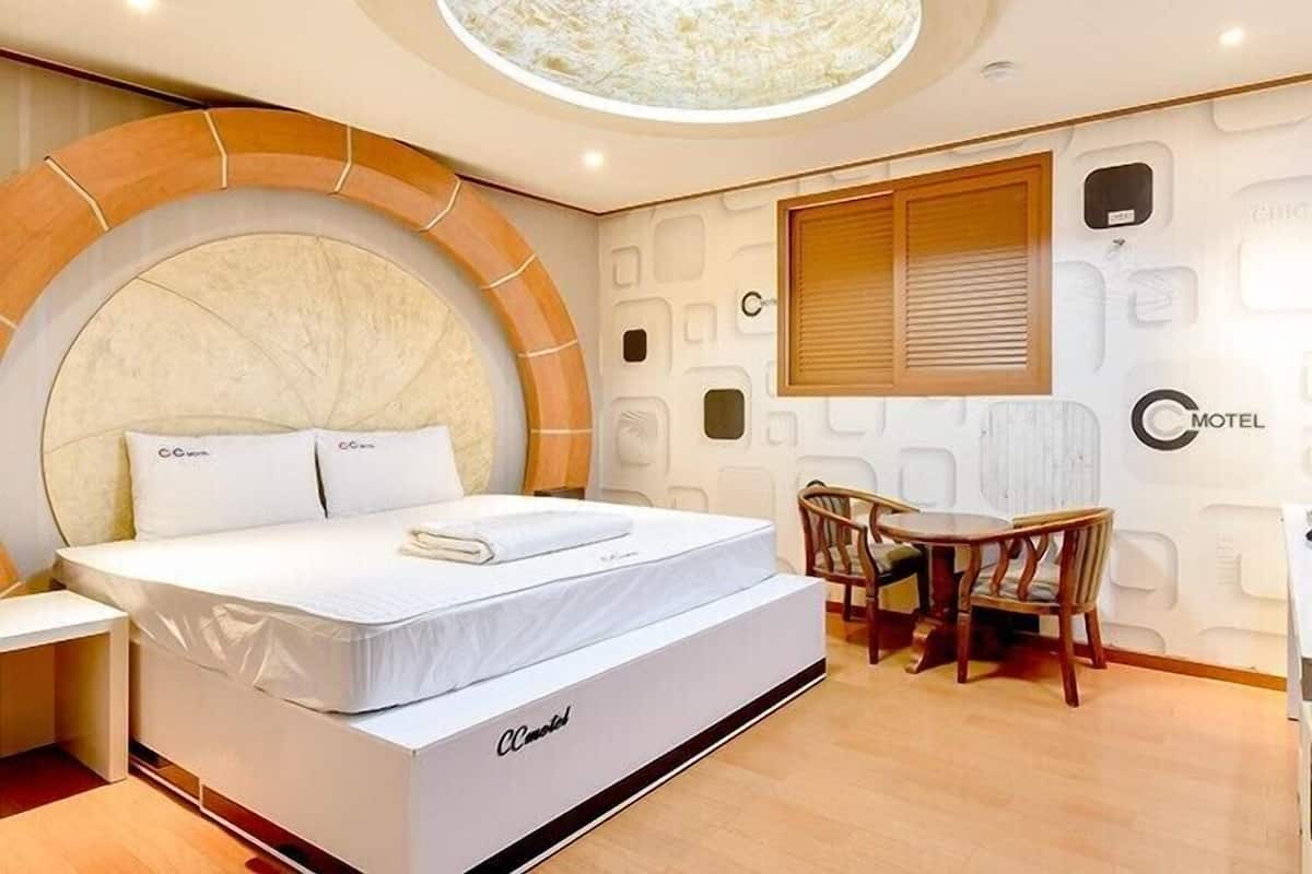Ein modernes Hotelzimmer mit einem großen Bett, einem Essbereich mit Tisch und Stühlen sowie einem außergewöhnlichen Deckengestaltung.