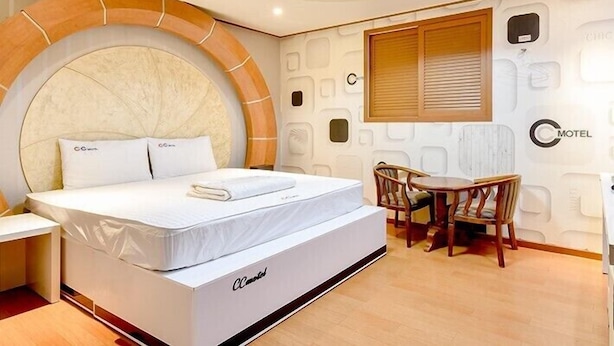 Une chambre d’hôtel moderne dotée d’un grand lit, d’un coin repas avec une table et des chaises, et d’un plafond au design original.