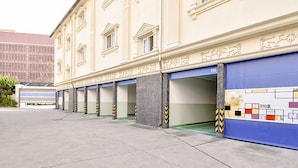 Une rangée de portes de garage fermées, avec une façade d’immeuble présentant une architecture classique et des moulures décoratives.