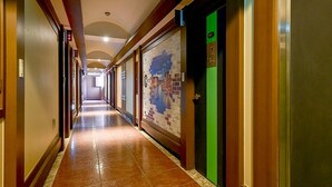 Un long couloir étroit, typique d’un hôtel, avec un sol carrelé et des murs recouverts de lambris en bois.
