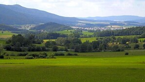 Ländliche Landschaft mit sanften Hügeln, einer kleinen Siedlung und wolkenlosem Himmel.