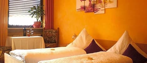 A room with two beds, a window with blinds, a potted plant, and a painting on the wall.