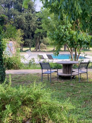 An outdoor seating area with a pool, surrounded by lush greenery and trees. - Mas Du Petit Claux (Barbentane)