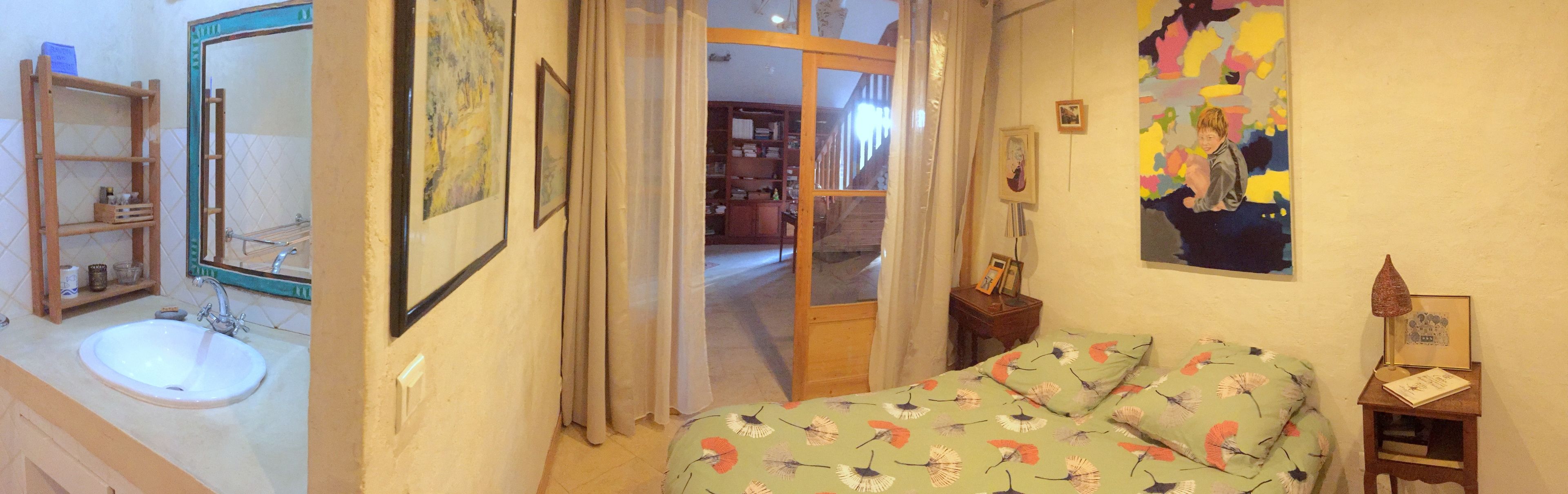 Une chambre à coucher avec un lit, une table de chevet, une lampe et un mur orné d’un tableau.