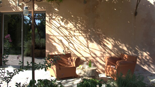 Un patio iluminado por el sol con dos sillones acolchados, una pequeña mesa redonda y un farol colgante.