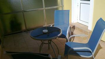 Een terras buiten met een ronde tafel en twee blauwe stoelen.