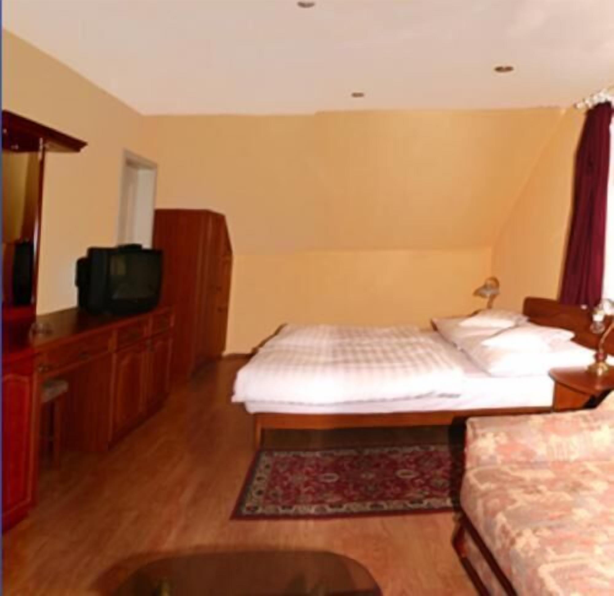 A bedroom with a bed, a desk with a television, a wardrobe, and a rug.