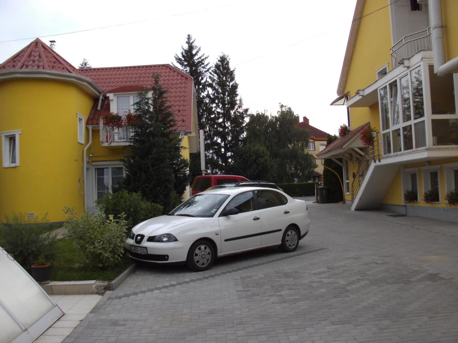 A white car parked in a driveway between two yellow buildings with red roofs.