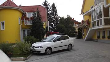 A white car parked in a driveway between two yellow buildings with red roofs.