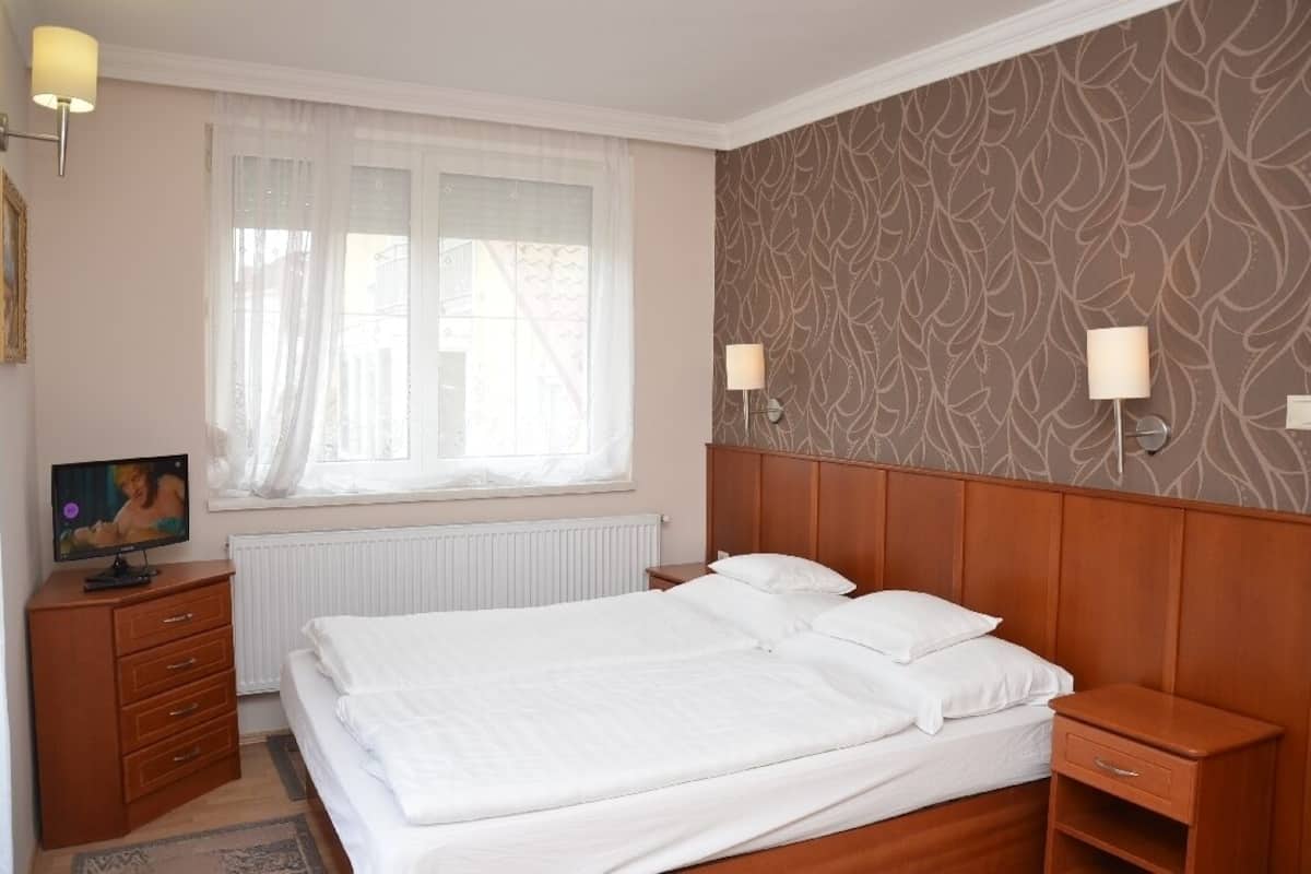Ein Hotelzimmer mit einem Bett, einem Schminktisch, einem Fenster mit durchsichtigen Vorhängen und einer Wand mit Muster.