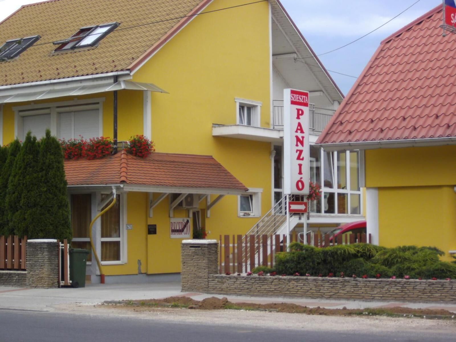 A yellow building with a red roof, a sign reading "PANZIO", and a small entrance with a wooden fence and potted plants.