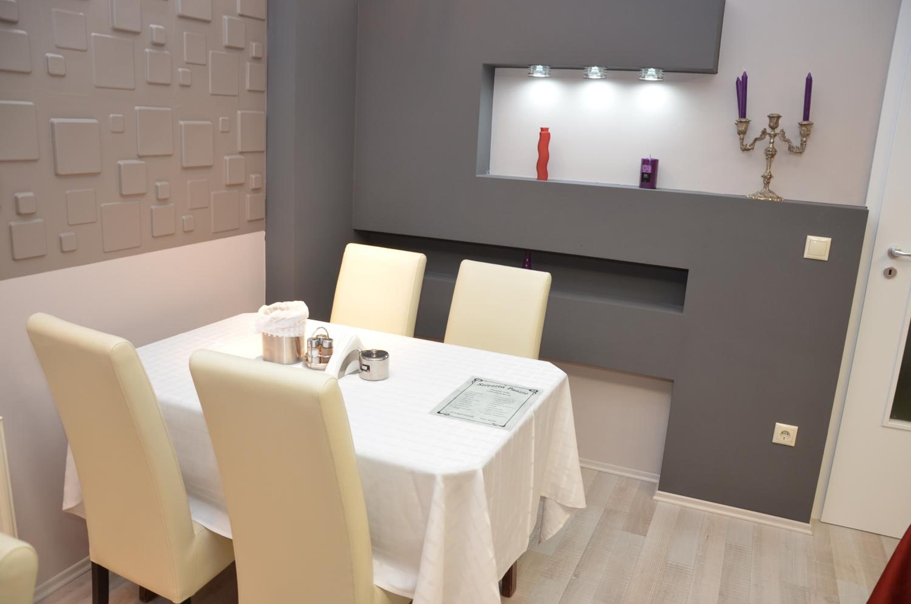 A dining area with a table set for four, a wall-mounted shelf with decorative items, and a grey accent wall.