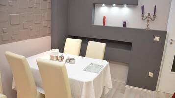 A dining area with a table set for four, a wall-mounted shelf with decorative items, and a grey accent wall.