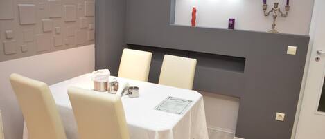 A dining area with a table set for four, a wall-mounted shelf with decorative items, and a grey accent wall.