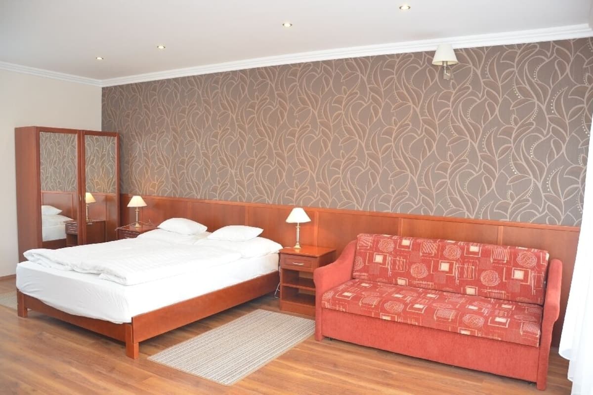 Ein Hotelzimmer mit einem hölzernen Bett, einem roten Sofa, einem Nachttisch mit Lampe und einer Wand mit Muster.