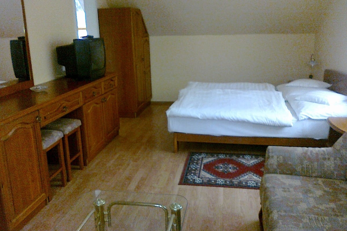 Ein Schlafzimmer mit einem Bett, einer Holzkommode, einem Fernseher und einem kleinen Tisch.