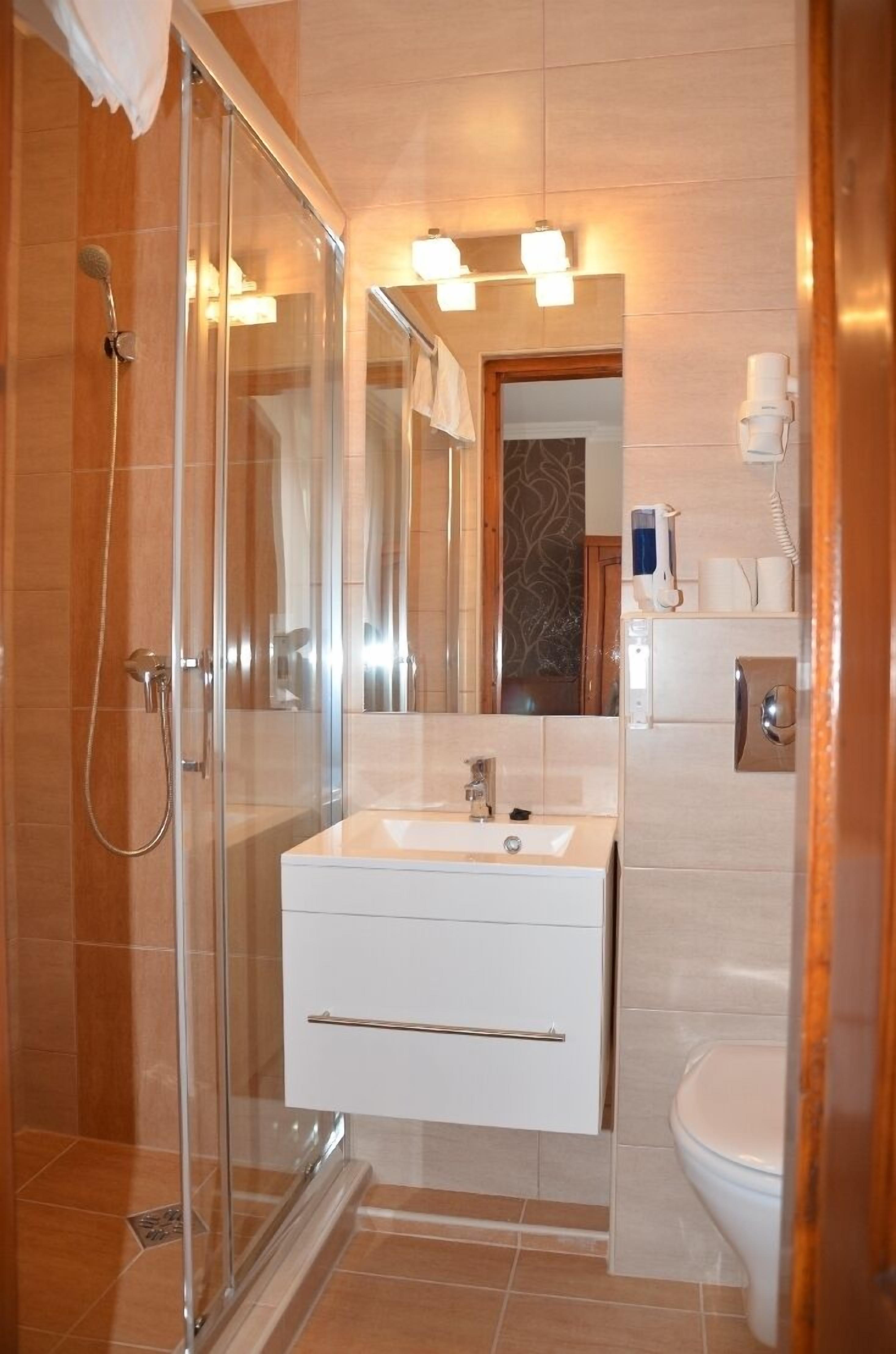 Un baño moderno con cabina de ducha de vidrio, un lavabo blanco y un espejo encima, además de un inodoro.