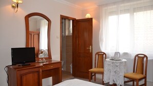 A hotel room with a bed, a desk with a TV, a mirror, a small table with chairs, and a window with sheer curtains. - Szieszta Panzió (Sarvar)