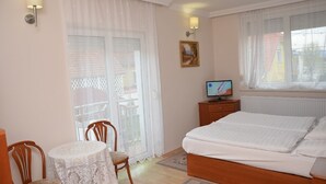 A bedroom with a bed, a TV, a table with chairs, and a window with curtains. - Szieszta Panzió (Sarvar)