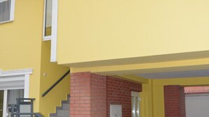 A two-story building with a yellow exterior, a brick base, and a white door. - Szieszta Panzió (Sarvar)