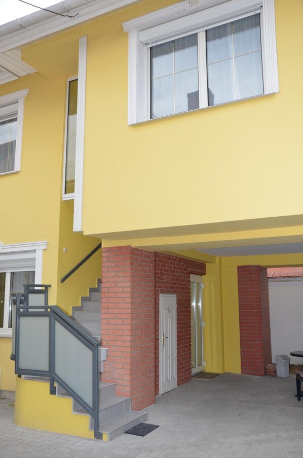 Un edificio de dos pisos con fachada amarilla, base de ladrillo y puerta blanca.