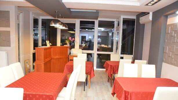 A restaurant with tables covered in red tablecloths, white chairs, and a wooden counter. - Szieszta Panzió (Sarvar)