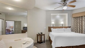 A hotel room with a large bed, a separate bathroom with a bathtub, a ceiling fan, and two bedside lamps. - Hilton Vacation Club The Falls Village Branson (Branson)