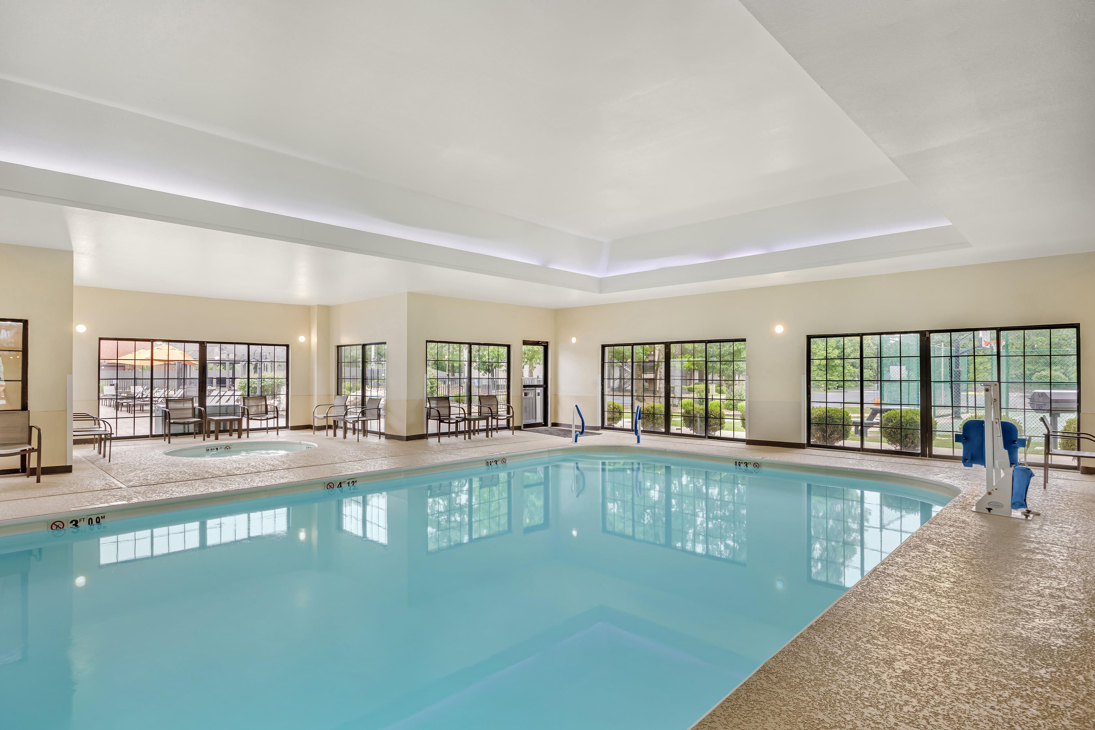 An indoor swimming pool with clear water, surrounded by lounge chairs and a view of the outdoors through large windows.