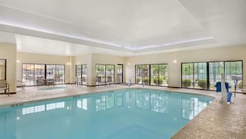 Una piscina interior con agua cristalina, rodeada de sillas de descanso y vistas al exterior a través de amplias ventanas.