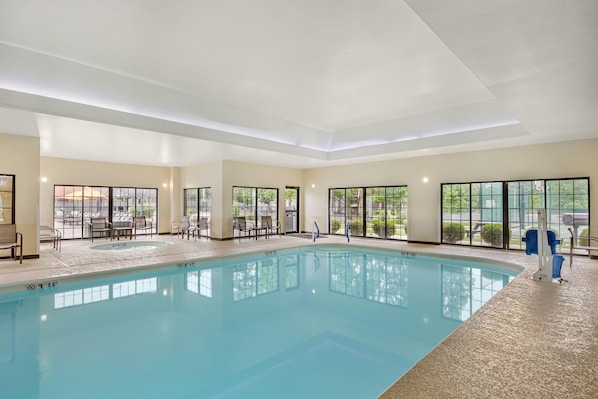 Una piscina interior con agua cristalina, rodeada de sillas de descanso y vistas al exterior a través de amplias ventanas.