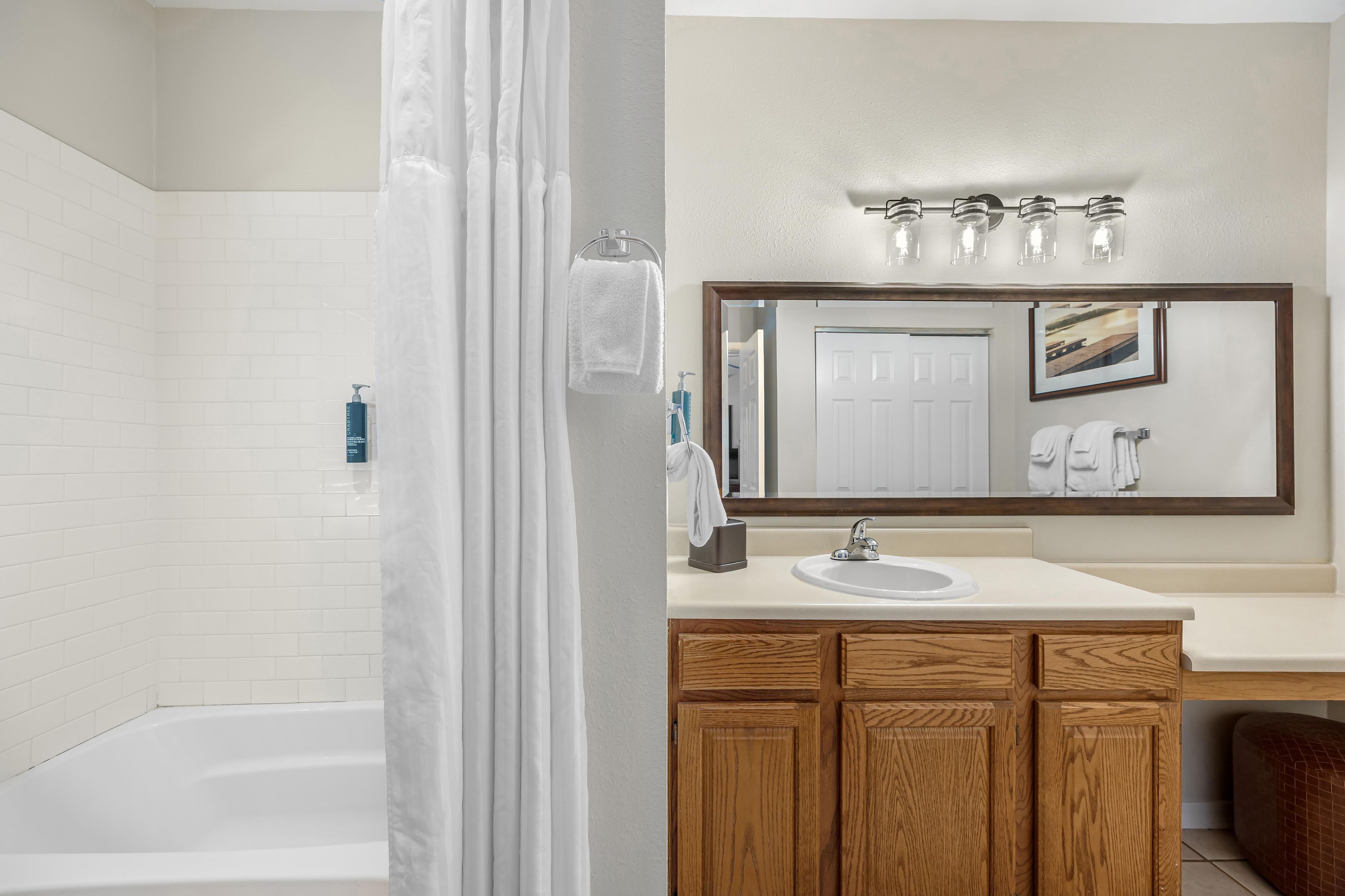 A bathroom with a bathtub, a sink, wooden cabinets, a mirror, and a shower curtain.