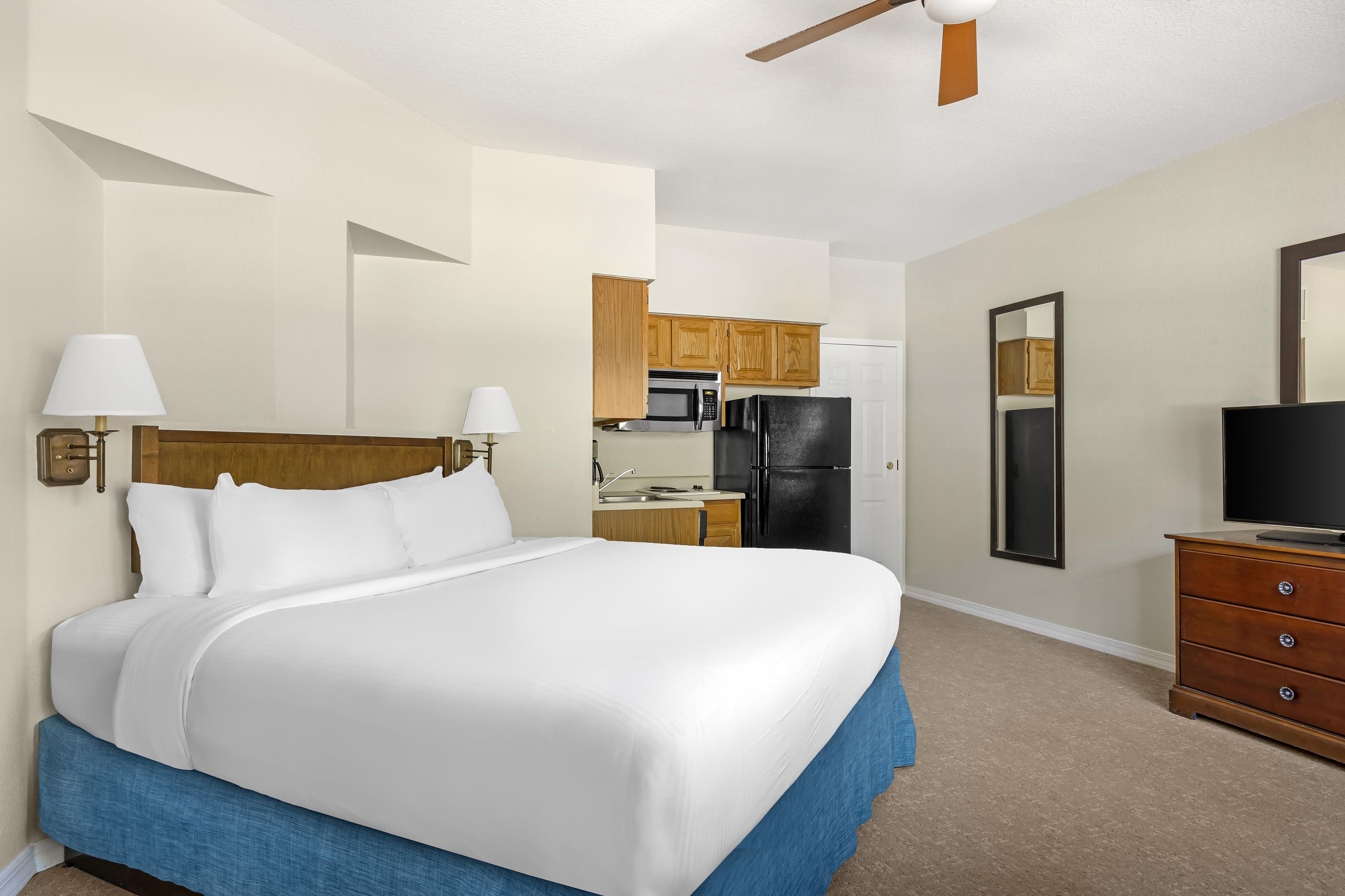 A hotel room with a bed, a desk, a refrigerator, a television, and a mirror.