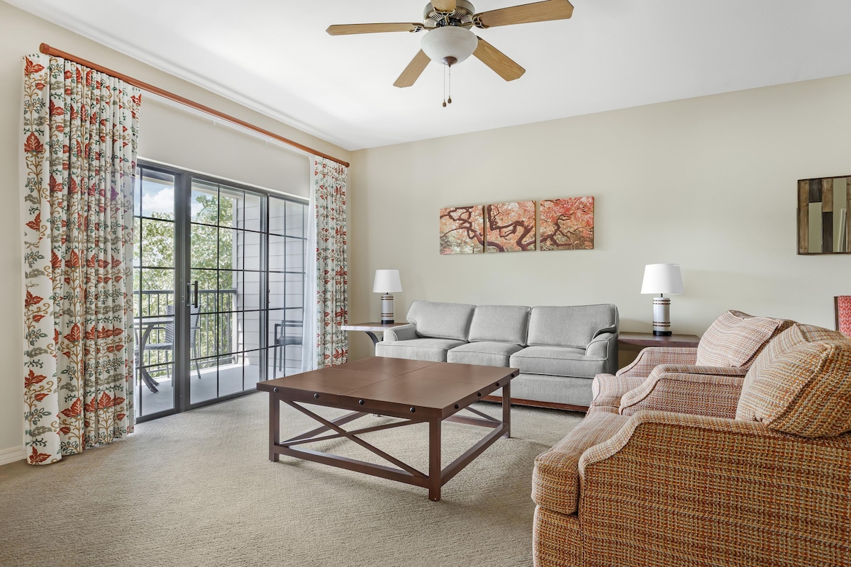 A living room with a ceiling fan, a sofa, a coffee table, and a large window with curtains.
