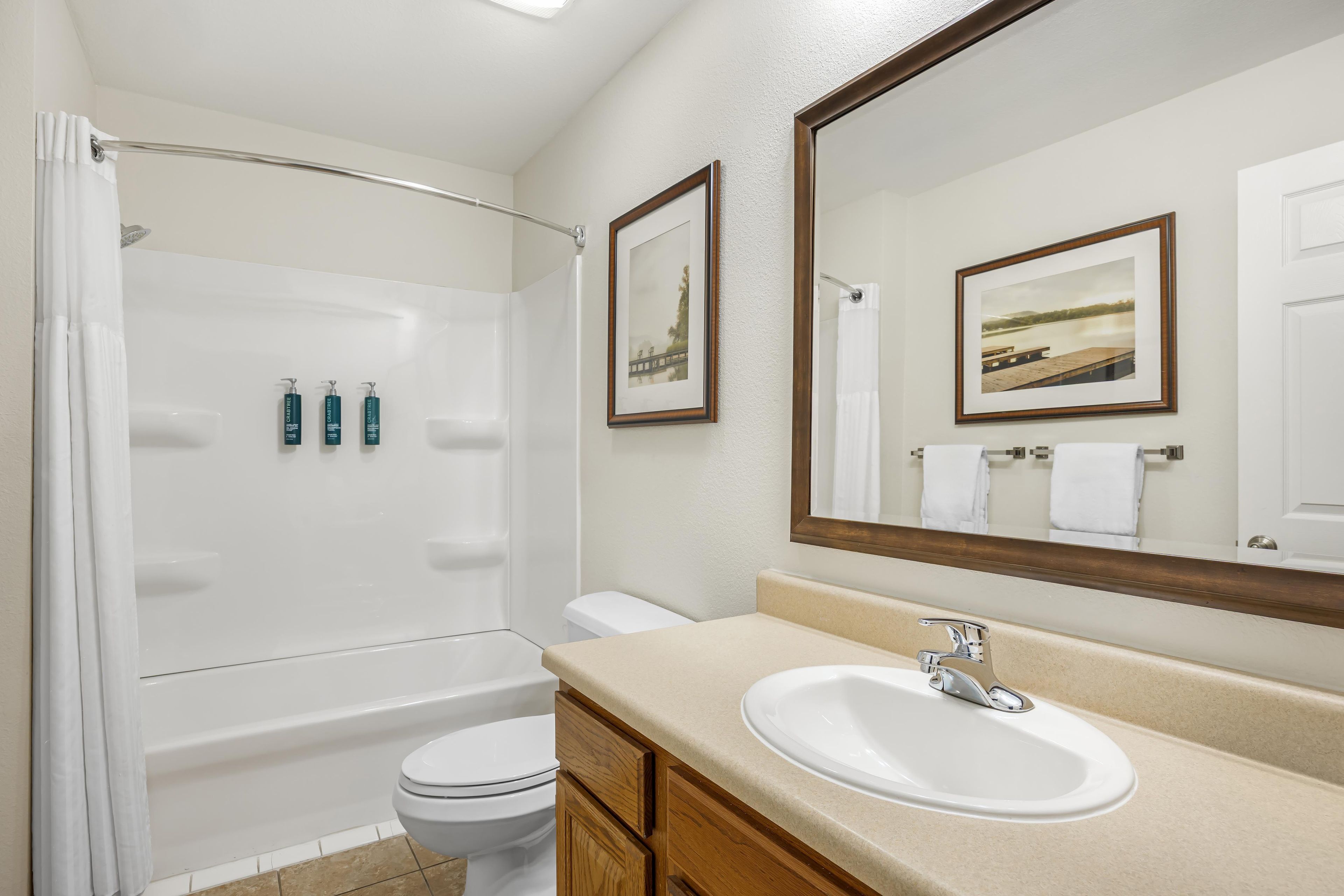 A bathroom with a bathtub, toilet, and sink. There are framed pictures on the wall.
