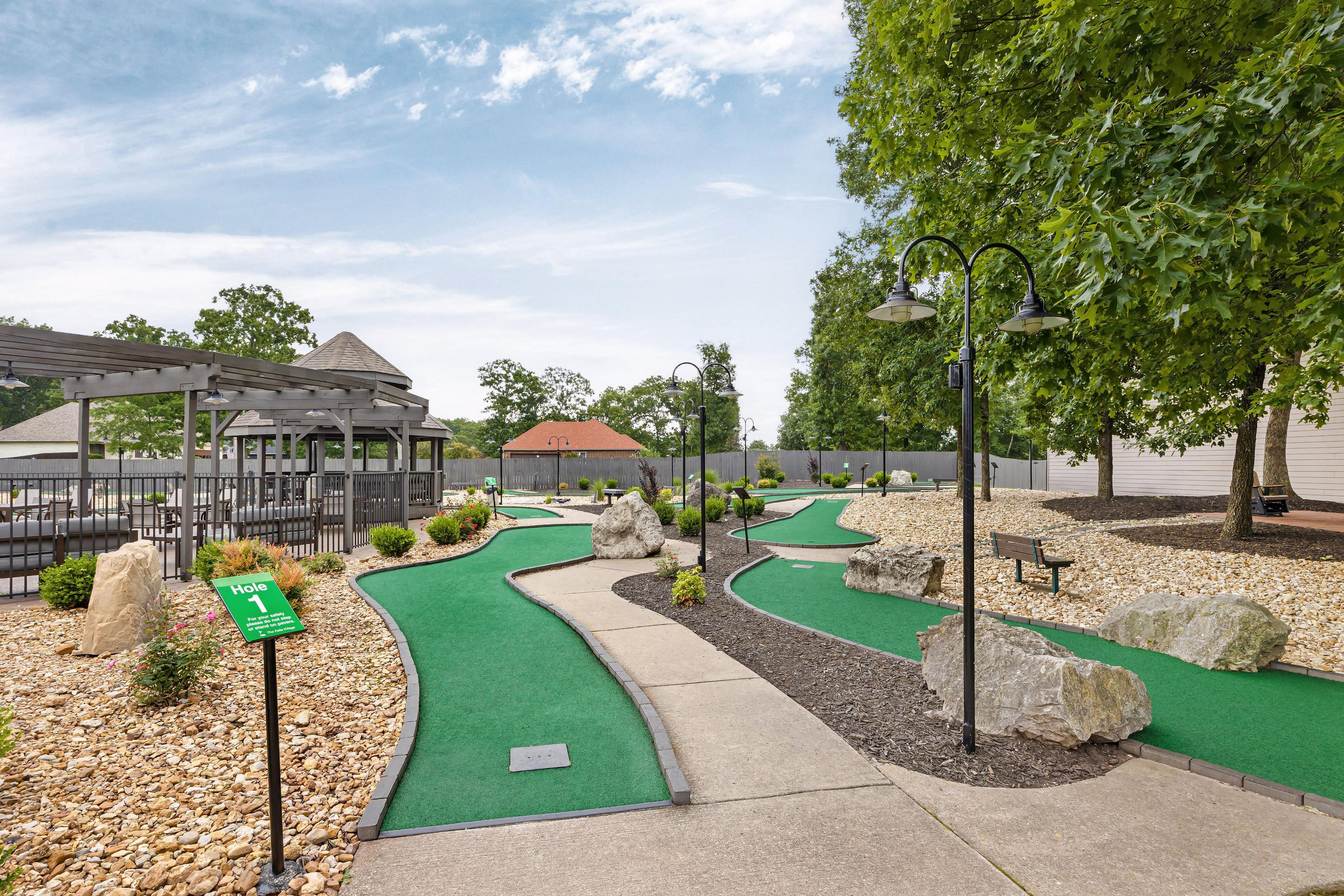 A miniature golf course with a gazebo, a sign indicating hole 1, and a pathway.