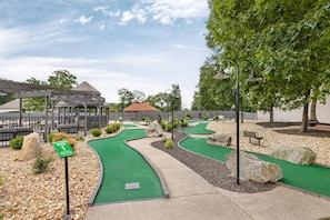 A miniature golf course with a gazebo, a sign indicating hole 1, and a pathway.