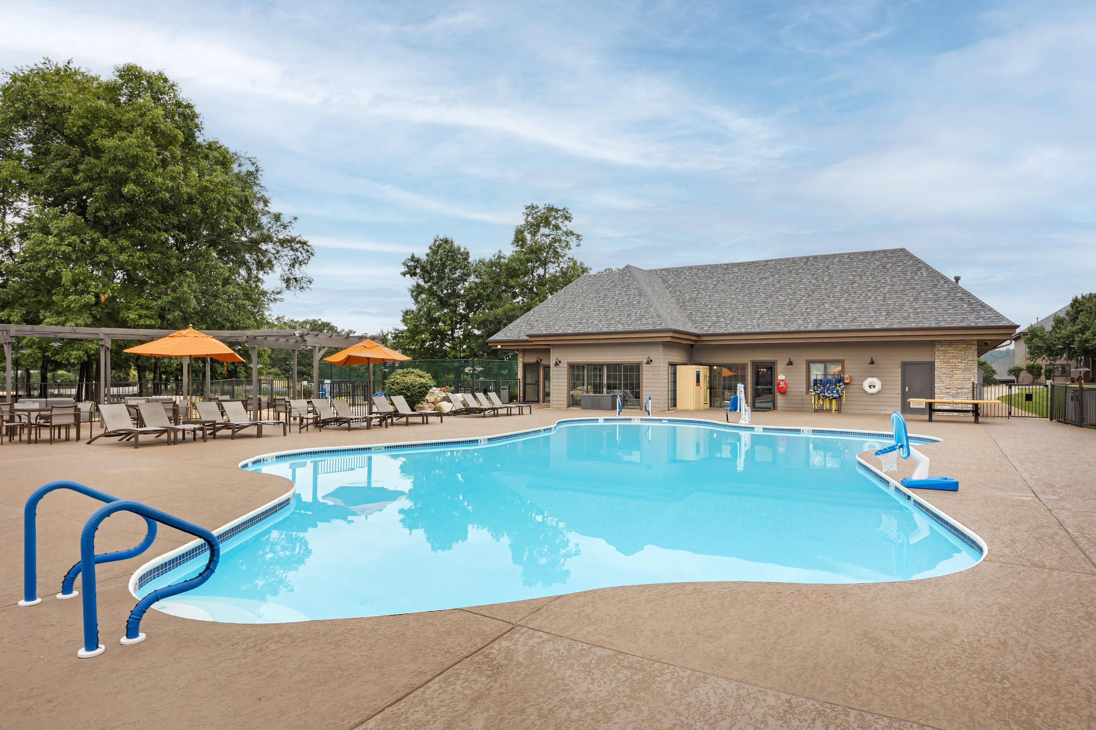 A swimming pool with lounge chairs and umbrellas, surrounded by a building with a tiled roof.