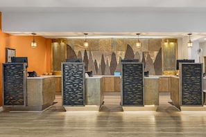 Zona de recepción de hotel con diseño moderno, que incluye una pared de piedra de fondo, mostradores de madera y luminarias colgantes.
