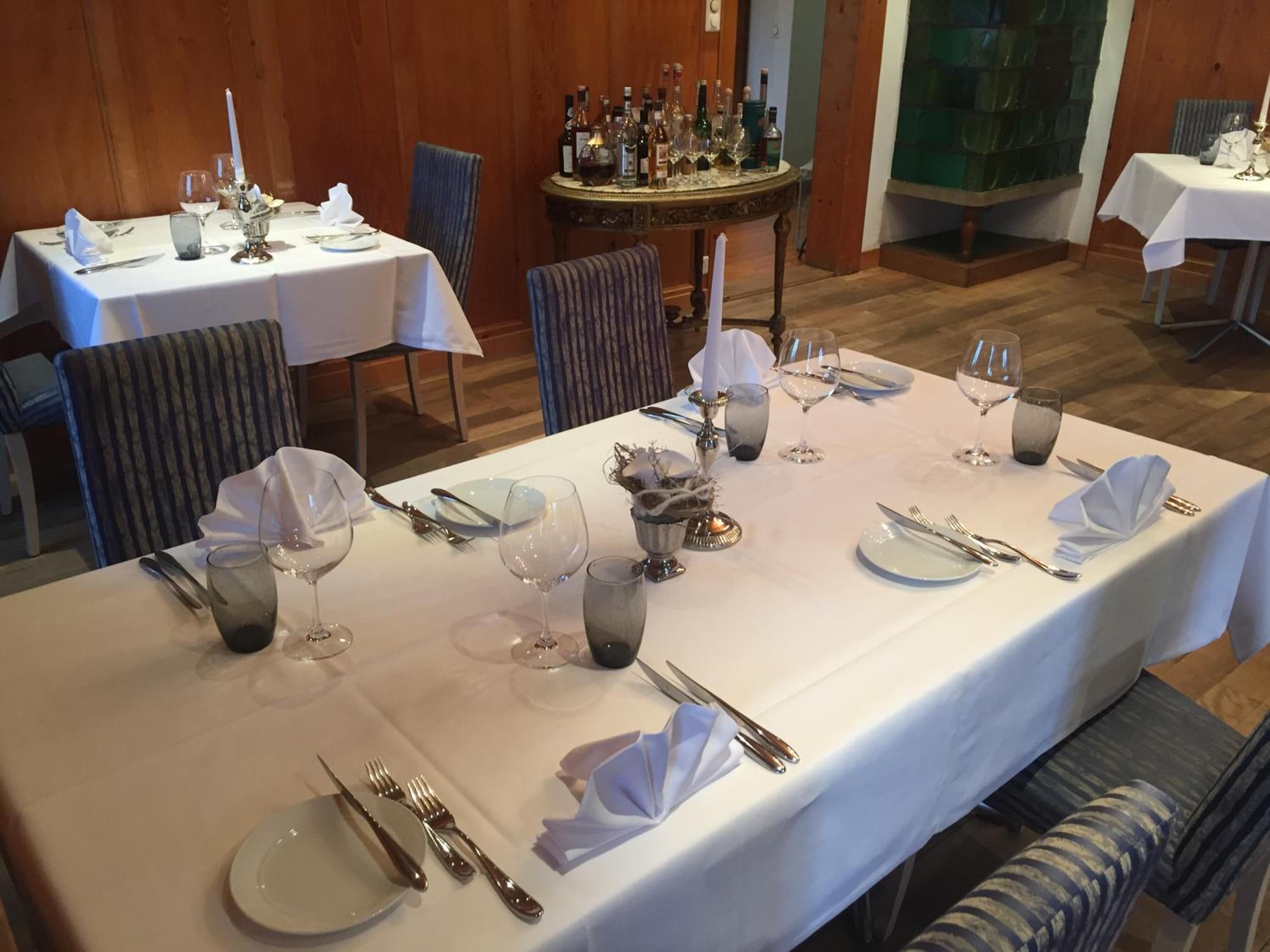 A dining area with tables set for a meal, featuring white tablecloths, silverware, and wine glasses.