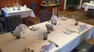 A dining area with tables set for a meal, featuring white tablecloths, silverware, and wine glasses.