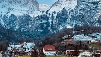 A mountain village with snow-covered peaks, houses with red roofs, and a clear sky.