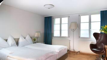 Une chambre d’hôtel avec un lit, une chaise, un bureau et une fenêtre avec des rideaux.