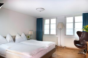A hotel room with a bed, a chair, a desk, and a window with curtains.
