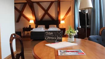 A hotel room with a wooden ceiling, a bed with white linens, a bedside table with a lamp, a small table with a vase of flowers, and a chair.